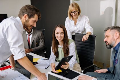 Equipe diversificada reunida em um escritório, colaborando diante de um tablet durante uma reunião.