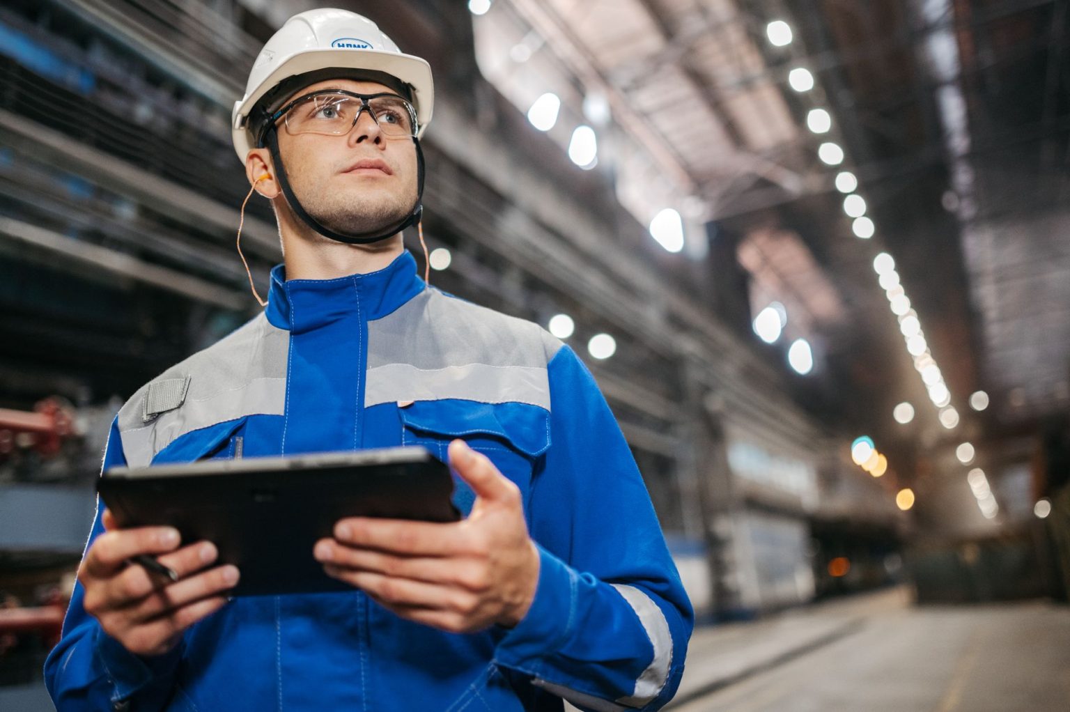 Trabalhador usando um tablet em um ambiente industrial, com equipamentos de segurança.