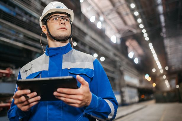 Trabalhador usando um tablet em um ambiente industrial, com equipamentos de segurança.