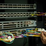 Mão organizando cabos de fibra óptica em uma sala de servidores.