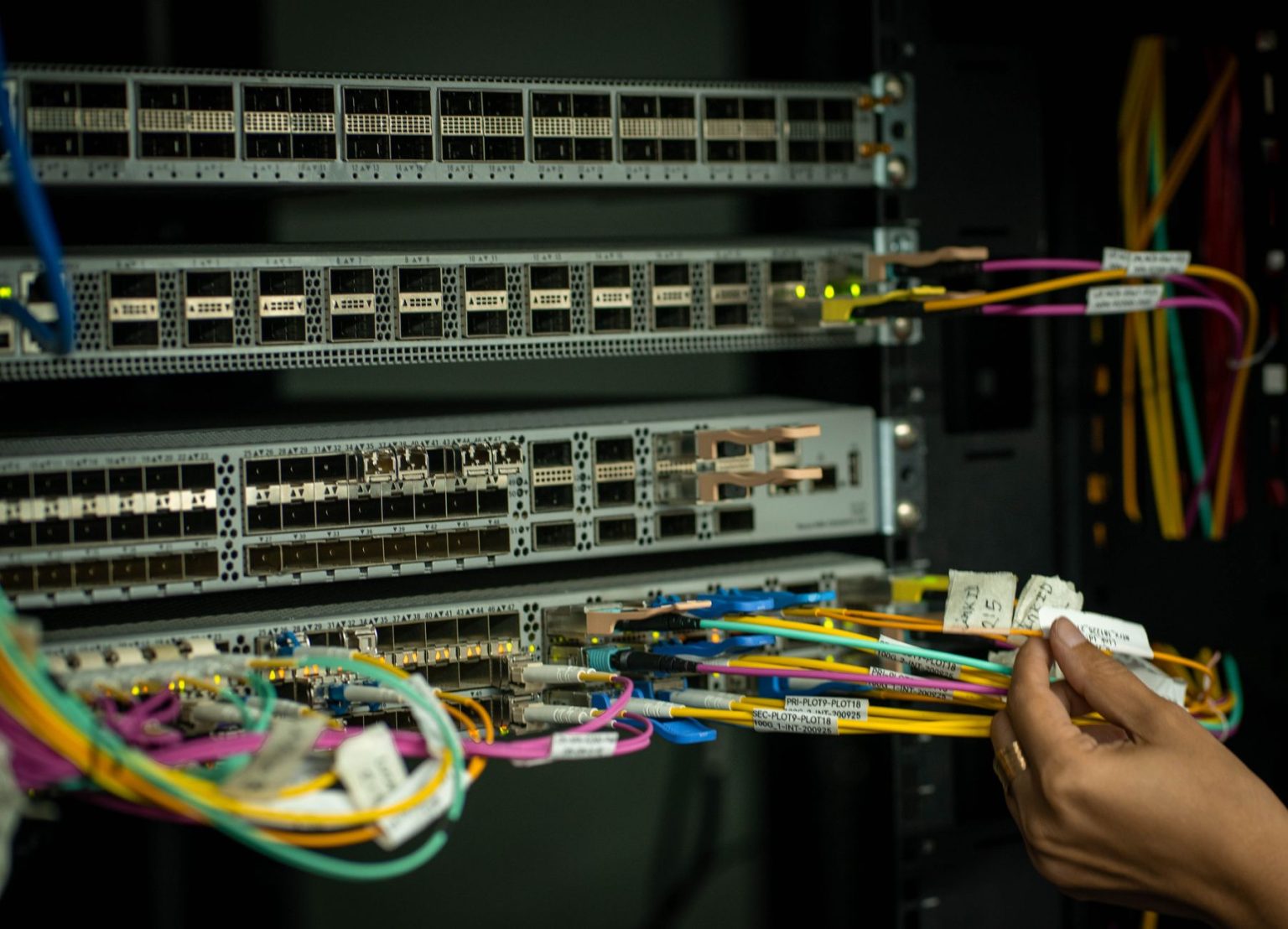 Mão organizando cabos de fibra óptica em uma sala de servidores.