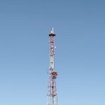 Torre de telecomunicações destacada contra um céu azul, representando a infraestrutura das redes móveis.