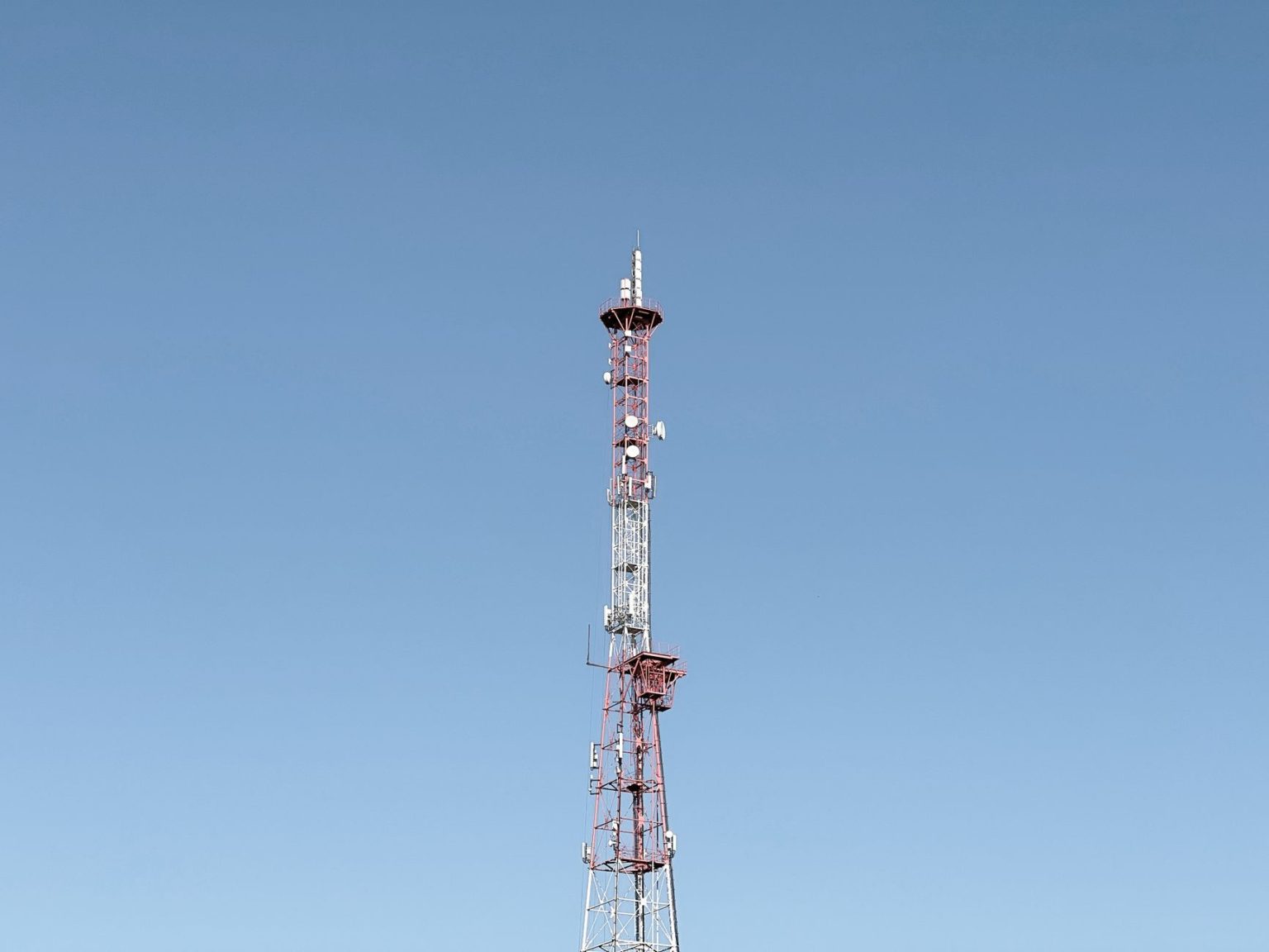 Torre de telecomunicações destacada contra um céu azul, representando a infraestrutura das redes móveis.