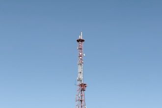 Torre de telecomunicações destacada contra um céu azul, representando a infraestrutura das redes móveis.