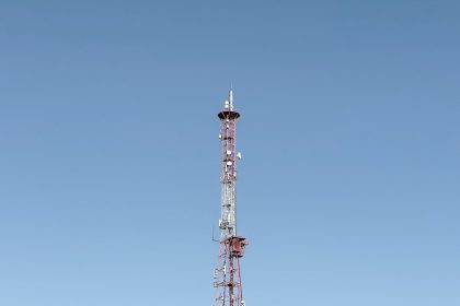 Torre de telecomunicações destacada contra um céu azul, representando a infraestrutura das redes móveis.