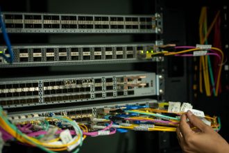 Mão organizando cabos de fibra óptica em uma sala de servidores.