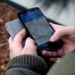 Mãos seguram um smartphone ao ar livre com um aplicativo de mapas e navegação por GPS aberto na tela.