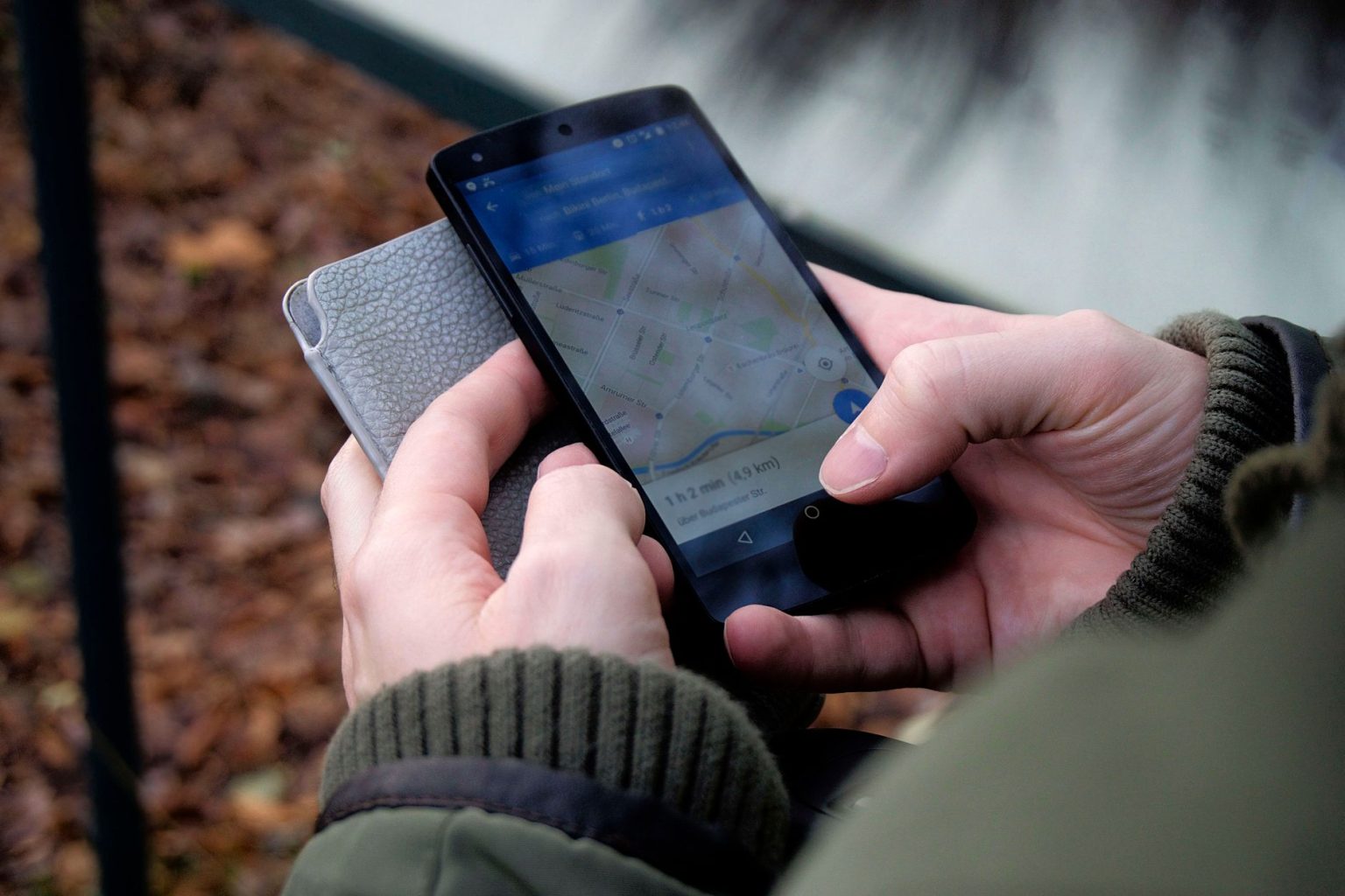 Mãos seguram um smartphone ao ar livre com um aplicativo de mapas e navegação por GPS aberto na tela.