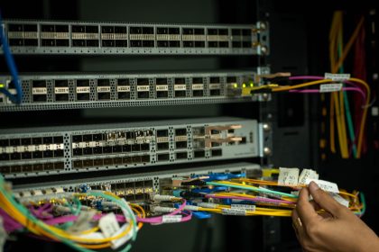 Mão organizando cabos de fibra óptica em uma sala de servidores.