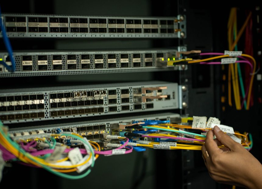 Mão organizando cabos de fibra óptica em uma sala de servidores.