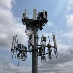 Torre de telecomunicações equipada com diversas antenas sob um céu nublado.
