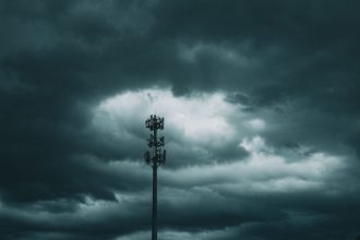Torre de telefonia celular isolada diante de um céu carregado de nuvens de tempestade.
