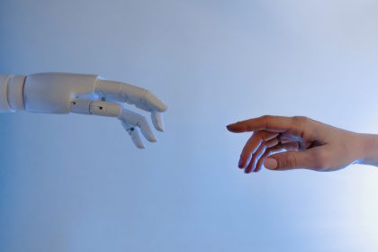 Mão humana estendida em direção a uma mão robótica, simbolizando a interação entre pessoas e inteligência artificial.